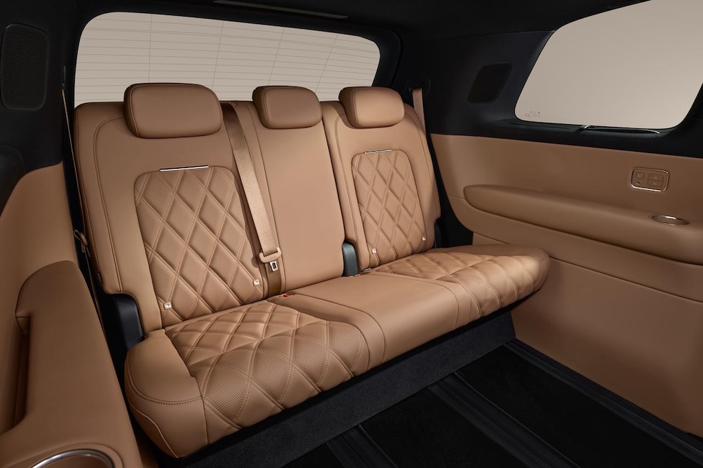 The back seat of the car is upholstered in brown leather, with seats designed with diamond stitching, a simple surrounding environment, and soft light filtering through the windows.