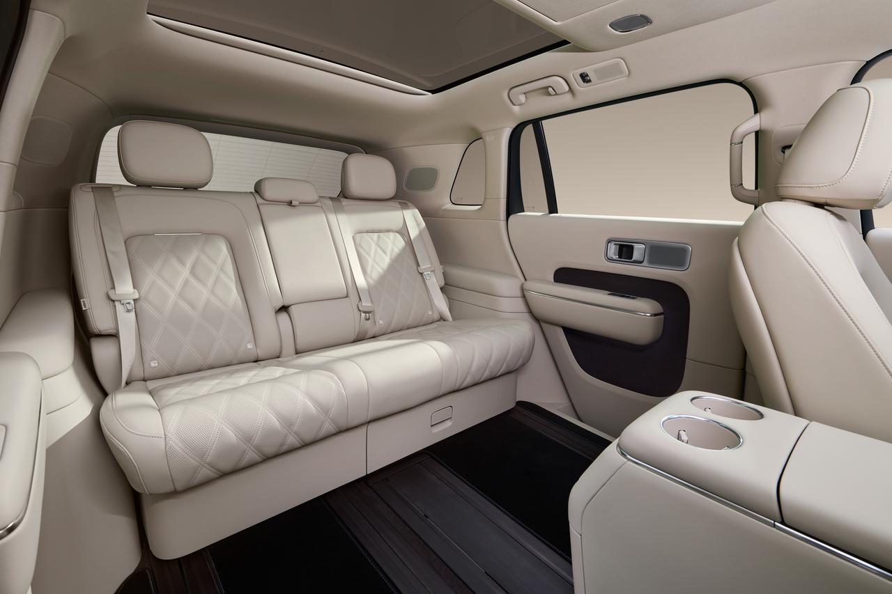 The interior of the back seat of the car features light-colored leather seats with diamond patterns, accompanied by a central armrest and cup holders, all designed in a minimalist modern style.