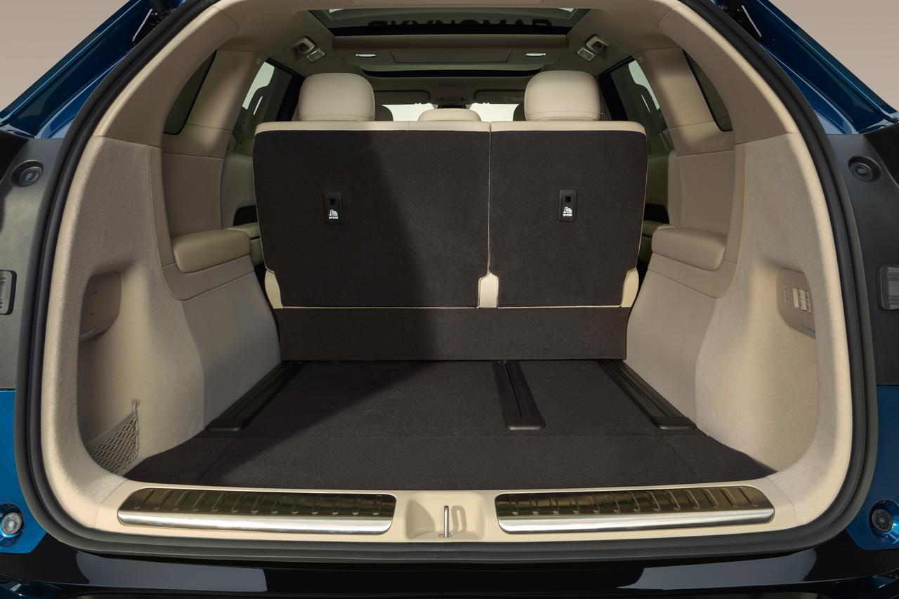 The interior of the car trunk has the backrest of the rear seat placed upright, with a flat black floor at the bottom and beige upholstery surrounding it, creating a spacious and bright environment.