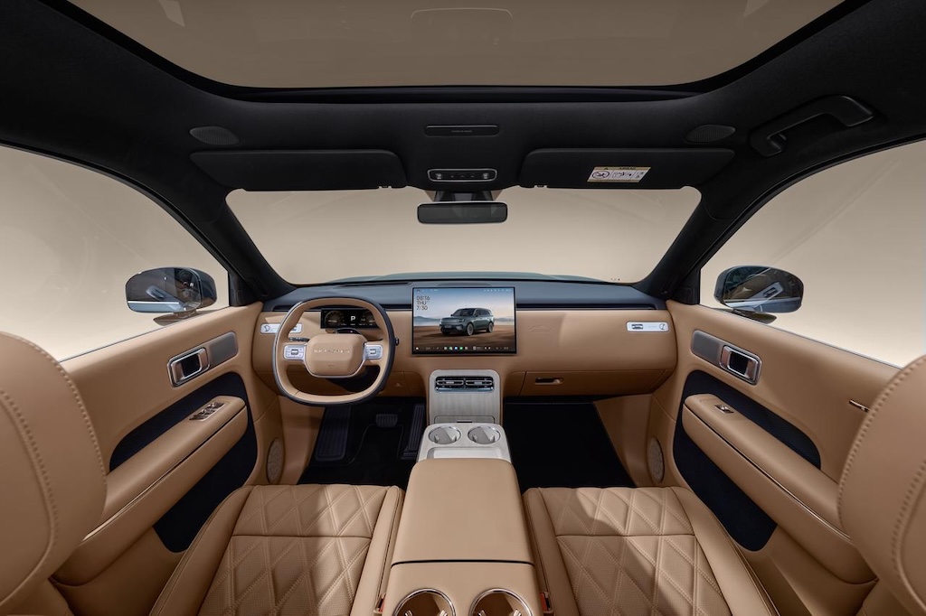 The in-car perspective showcases a luxurious interior, with light-colored leather seats and panels. A large screen displays information in the center, while the steering wheel and console have a modern design, creating an overall spacious and comfortable environment.