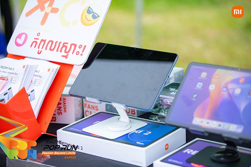 The booth showcased several tablet models, including the Redmi Pad 2, with promotional materials and slogans in the background, set in an outdoor environment.