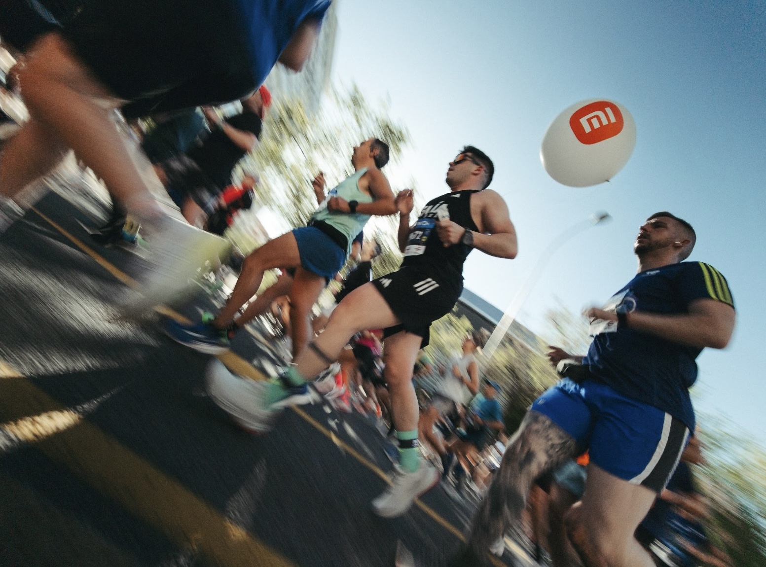 Many runners are participating in the marathon on the streets, with a backdrop of blue skies and trees, creating a lively scene.