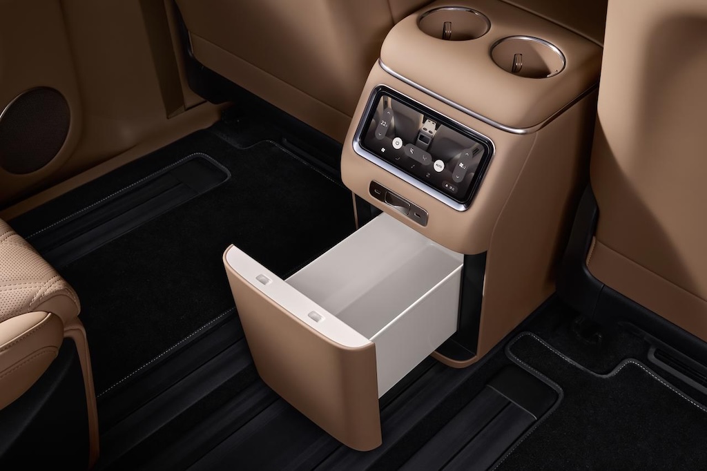 The central armrest area of the car is equipped with two cup holders and a pull-out storage drawer, with a background of dark carpet and beige interior.