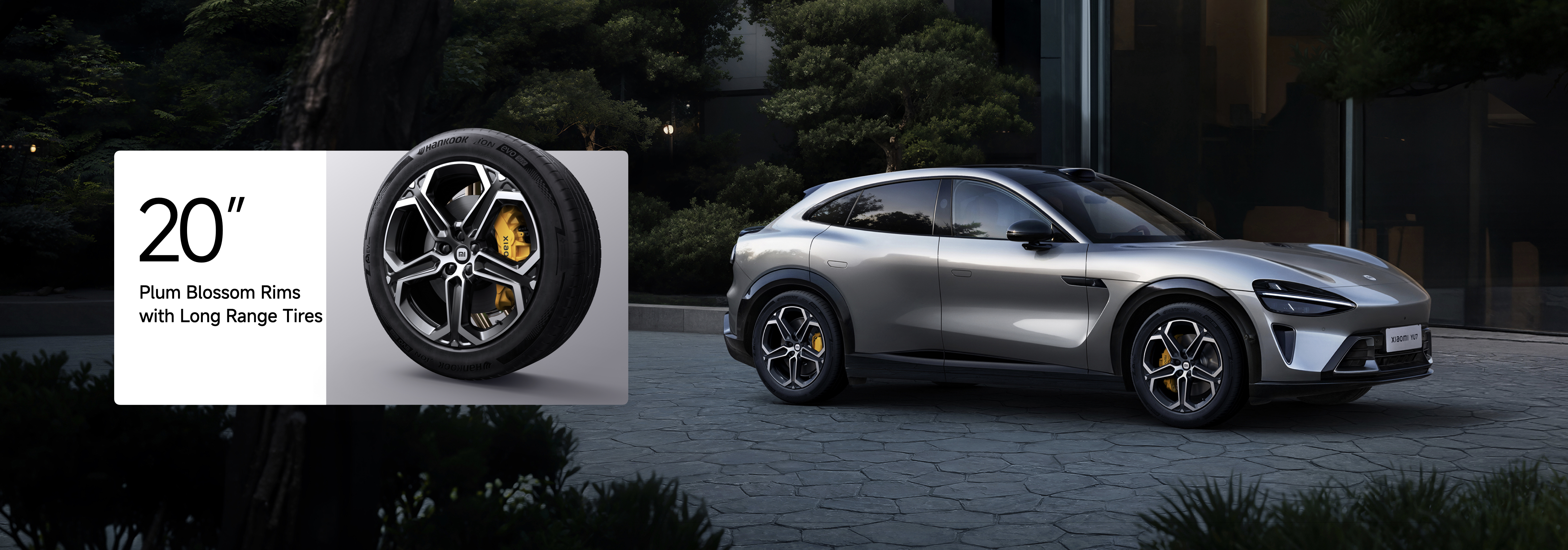 A silver car is parked on the cobblestone road, next to it is a display of a 20-inch wheel, featuring a star-shaped rim and long-lasting tires, with a background of green trees and buildings.