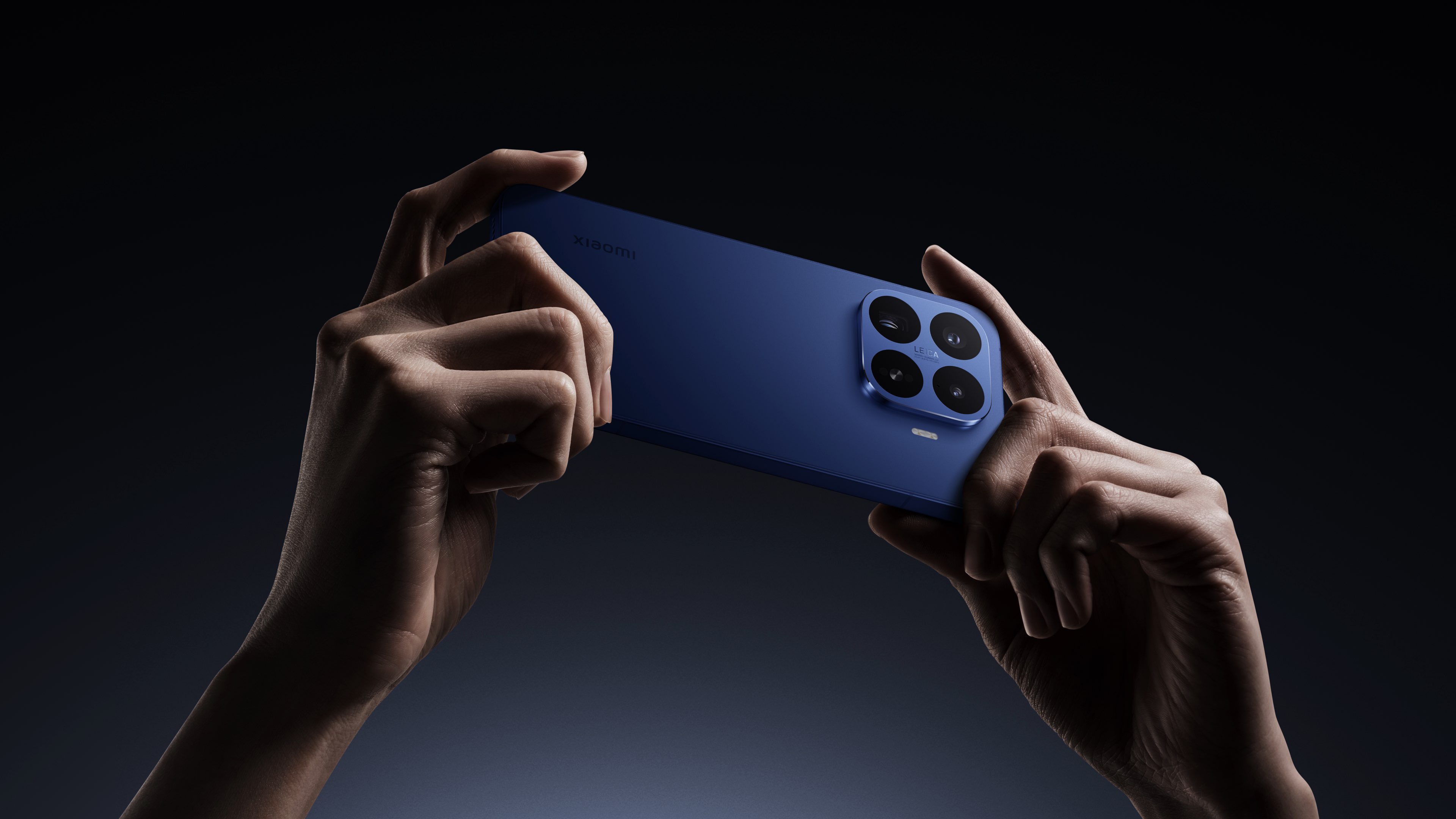Una mano sostiene un teléfono azul, la parte trasera del teléfono tiene cuatro cámaras y el fondo es un degradado oscuro.