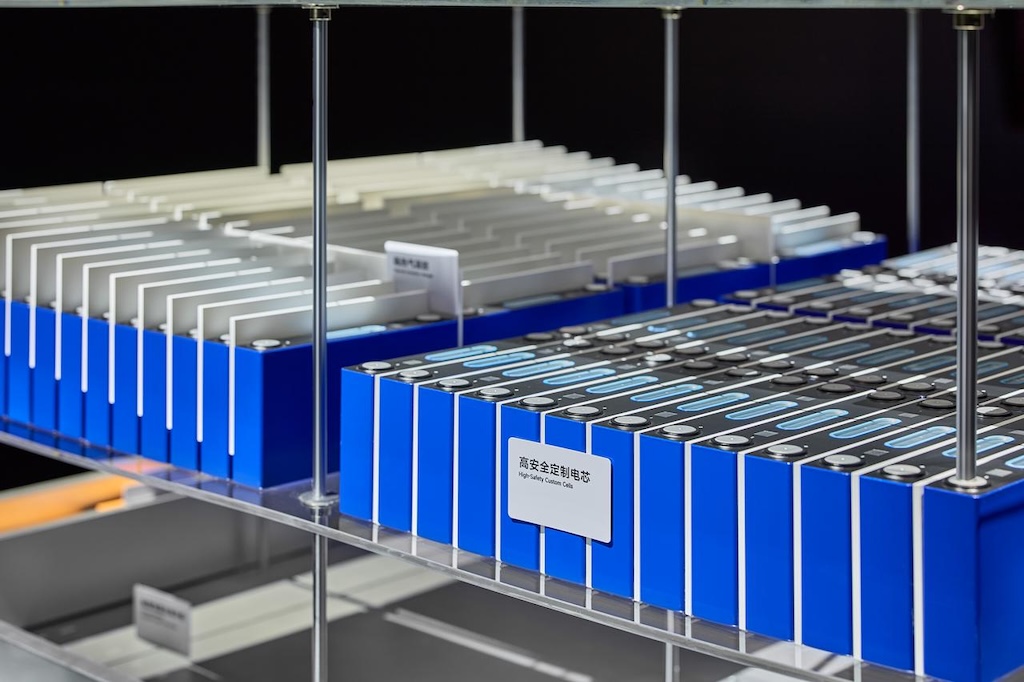 It shows a shelf with multiple rows of batteries in different colors, mainly blue and white, with a label that says "High Safety Control Cells." The background may be black, highlighting the color and design of the batteries.