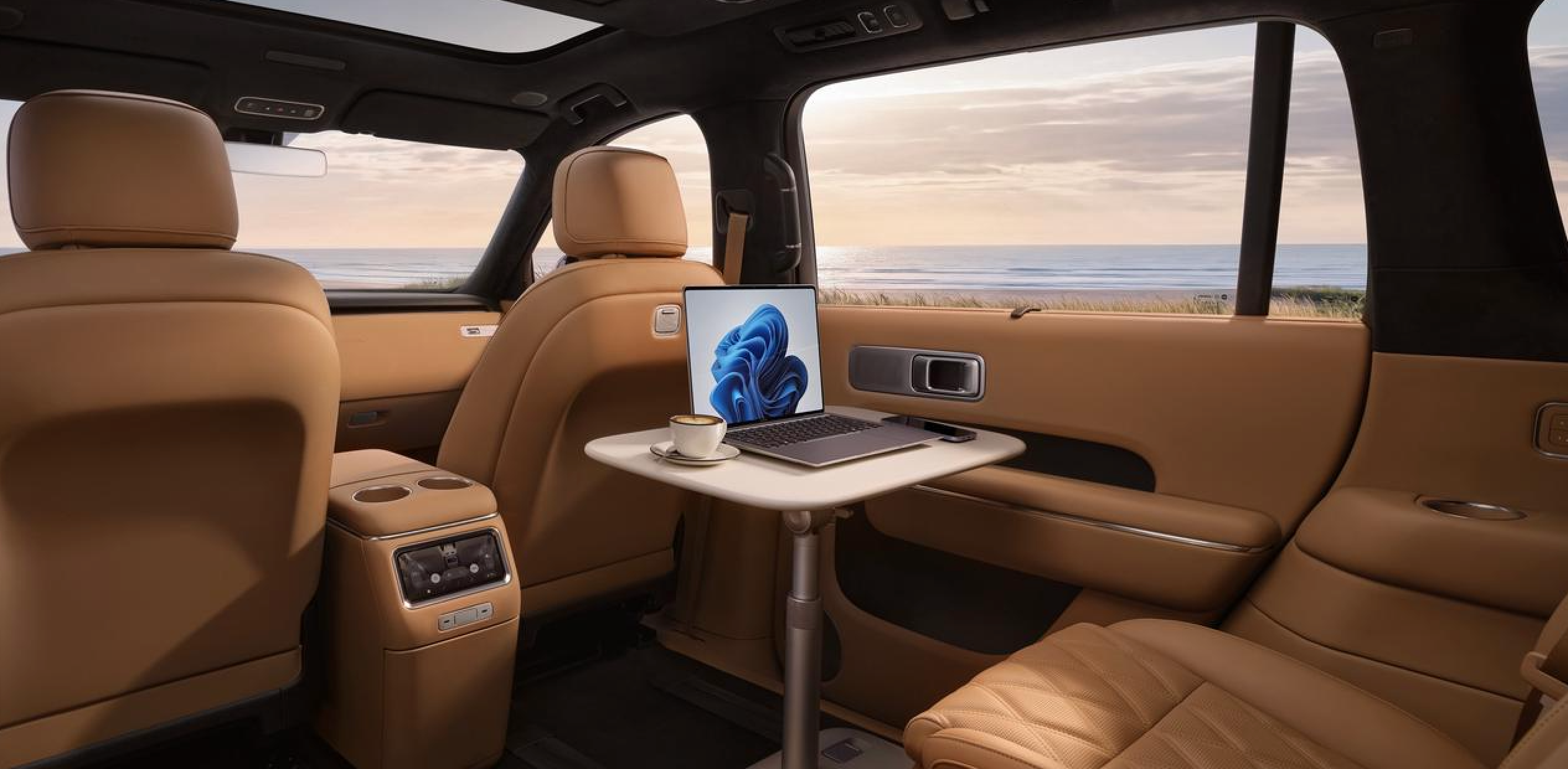 Luxurious car interior, brown leather seats, equipped with a computer and a coffee cup, with a view of the beach and ocean outside, the environment is peaceful and comfortable.