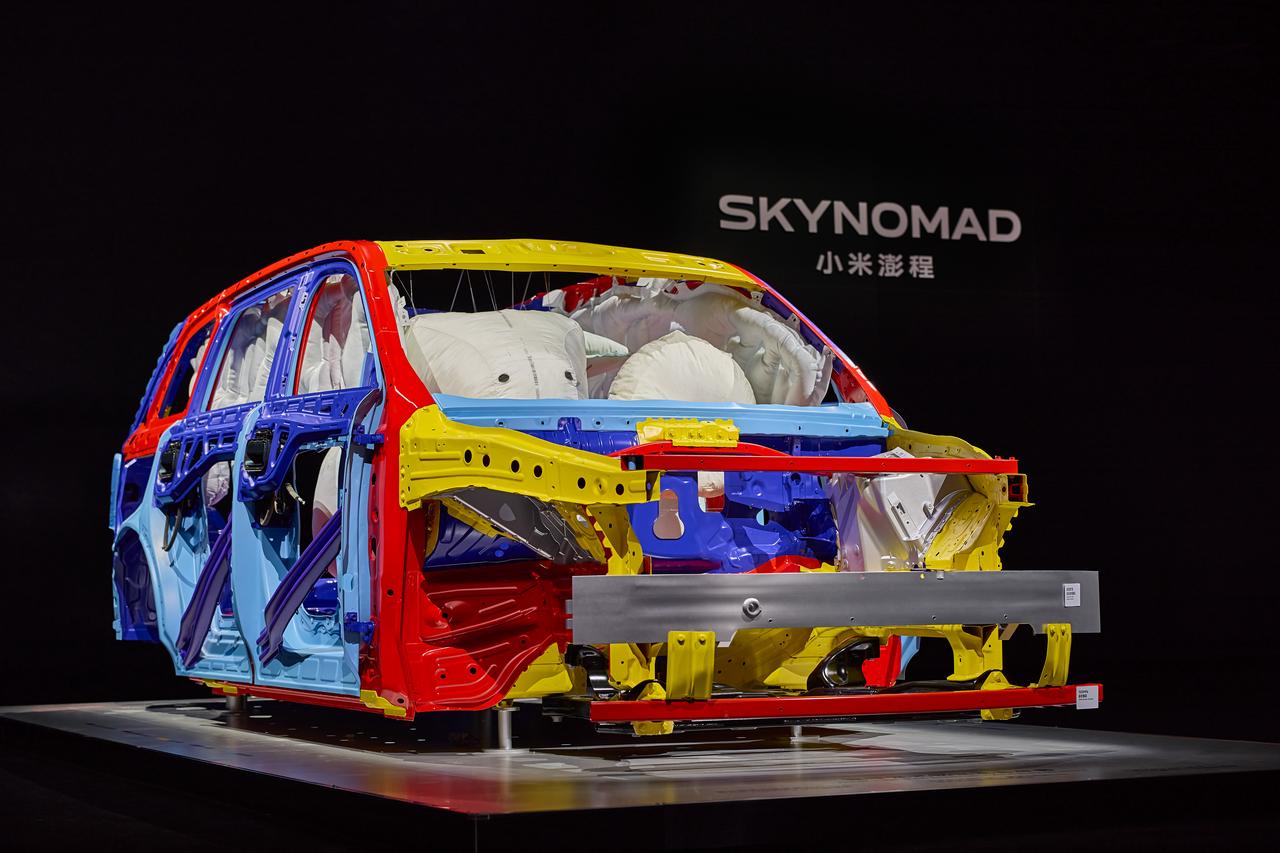 A colorful car frame is displayed, painted in red, blue, yellow, and white, with a black background, and the words "SKYNOMAD" and "Xiaomi Travel" next to it.