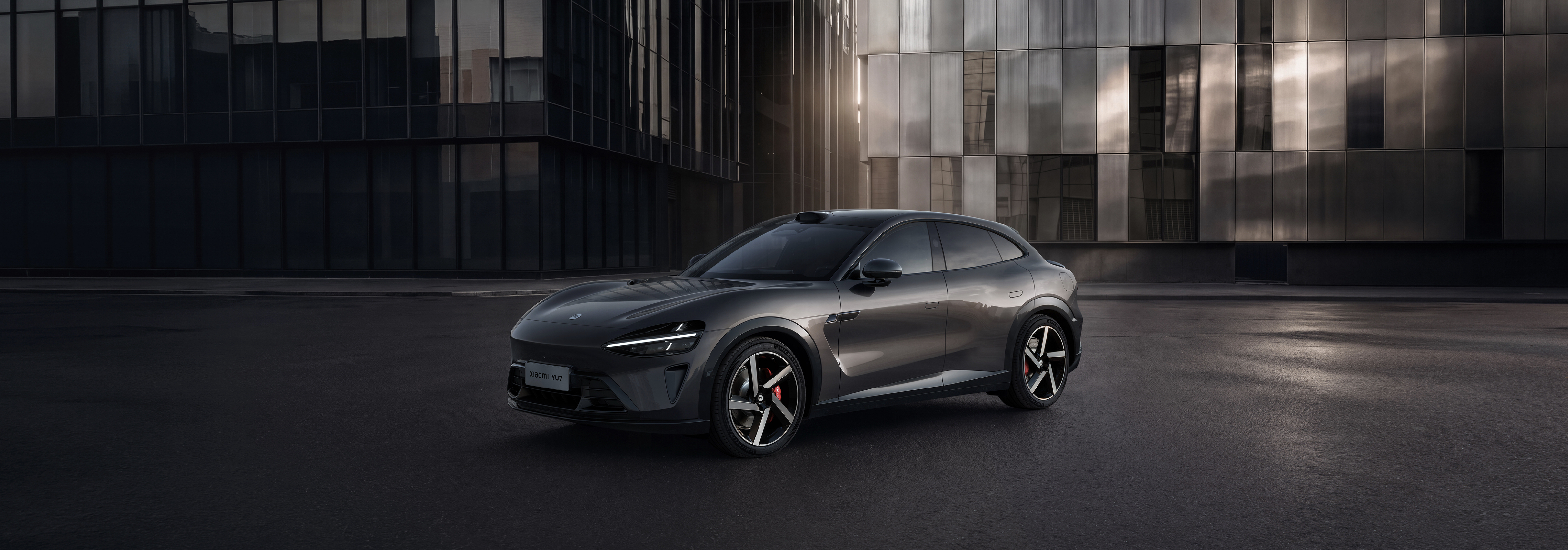 A gray sports car is parked on the city street, with modern glass curtain wall buildings in the background. The wheels have red brake calipers, and the overall design looks stylish and dynamic.