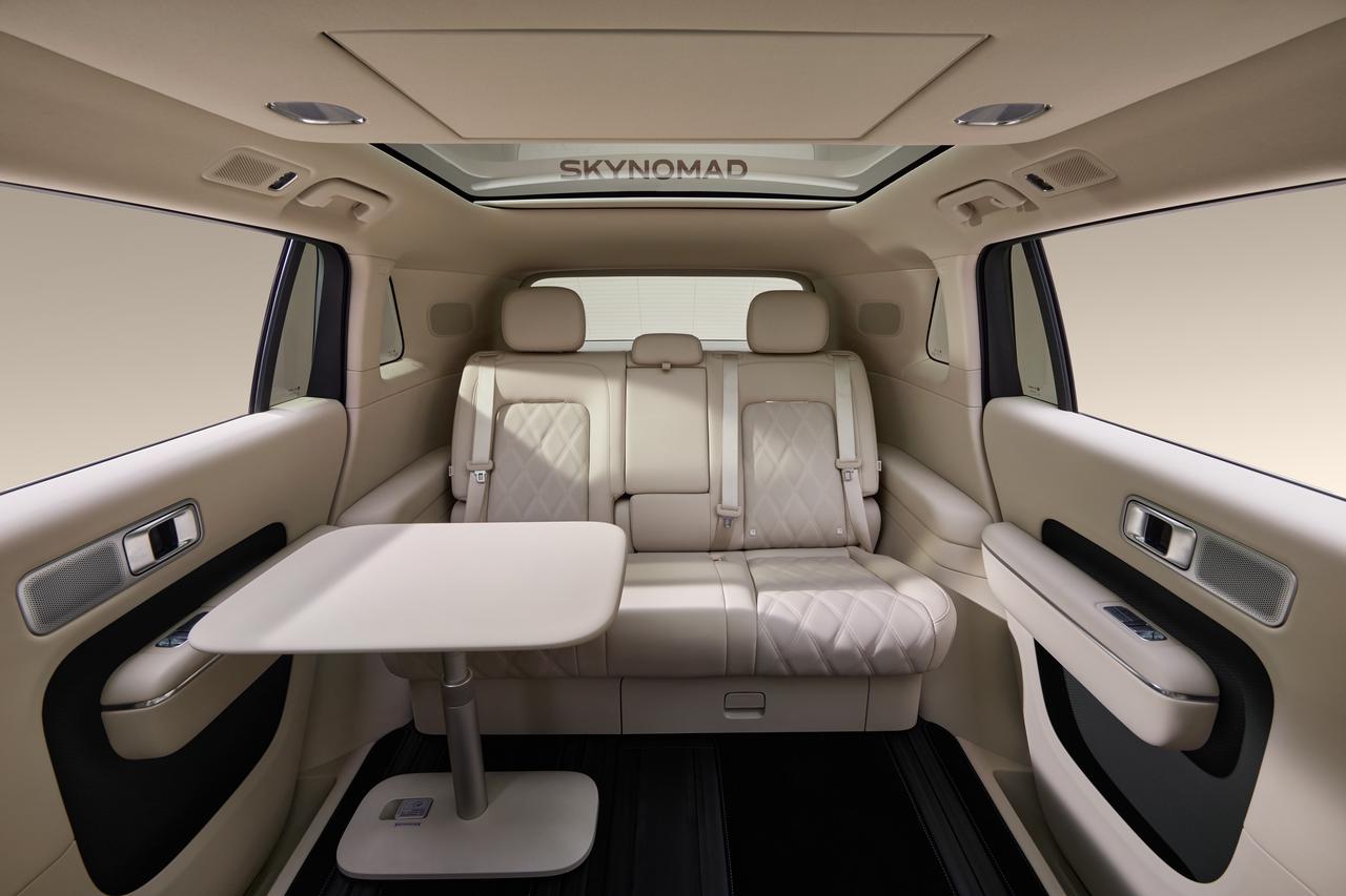 The interior of the car features beige leather seats and foldable tables, with a minimalist design on the walls and ceiling, including a sunroof. The overall style is modern and comfortable.