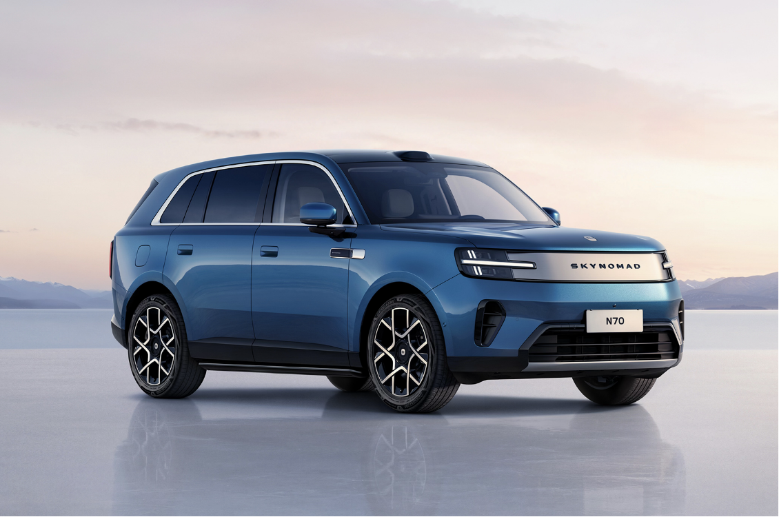 A blue SUV is parked on a smooth surface, with a soft sky and distant mountains in the background. The car's design is modern, and the front features the brand name "SKYMONAD N70."