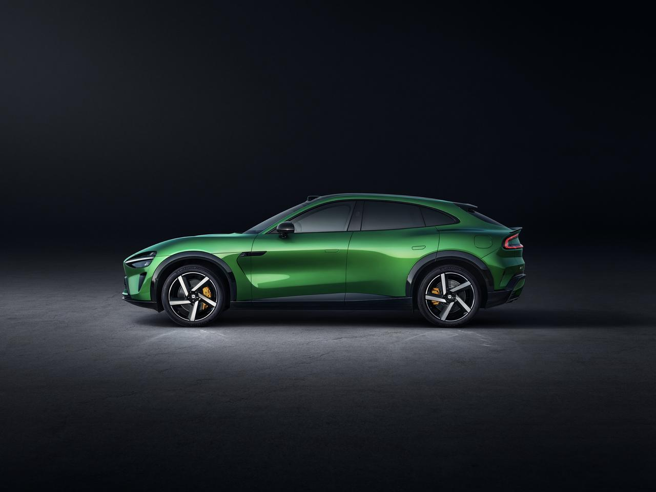 Vista laterale di un'auto sportiva verde, con uno sfondo scuro, che mostra il design aerodinamico del veicolo e le ruote sportive.