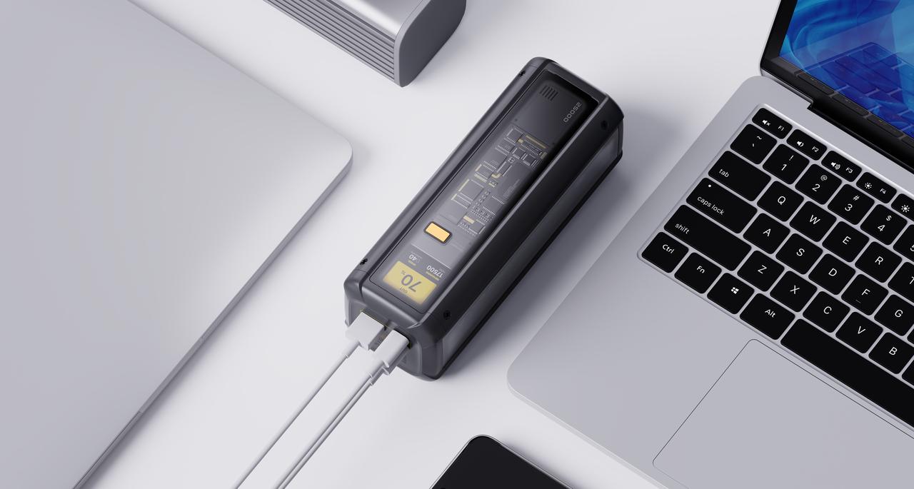 O dispositivo de carregamento está localizado ao lado do portátil, com números e botões exibidos no ecrã, ligado por cabos e rodeado por outros produtos eletrónicos.